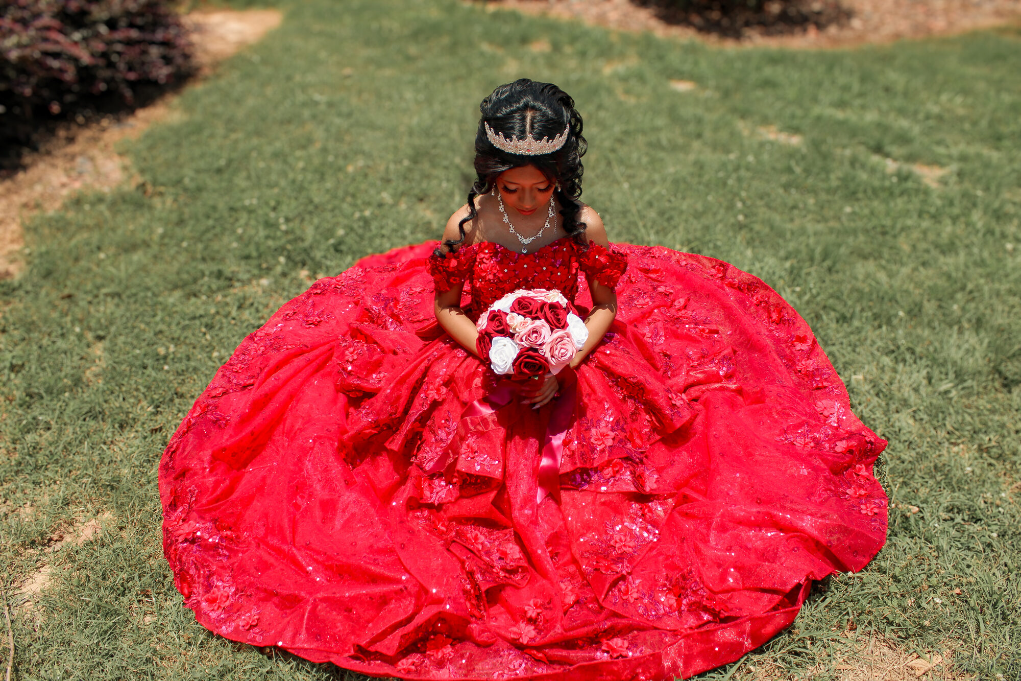 Quinceañera seated in the grass with a bouquet