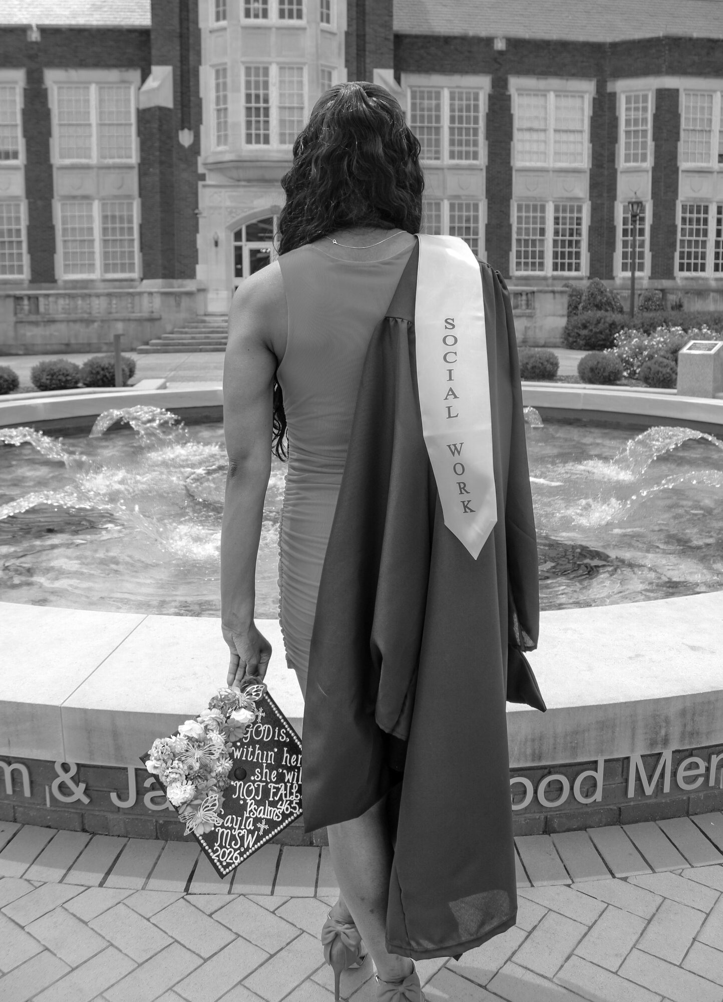 MSW graduate walking to a campus fountain with a decorated cap