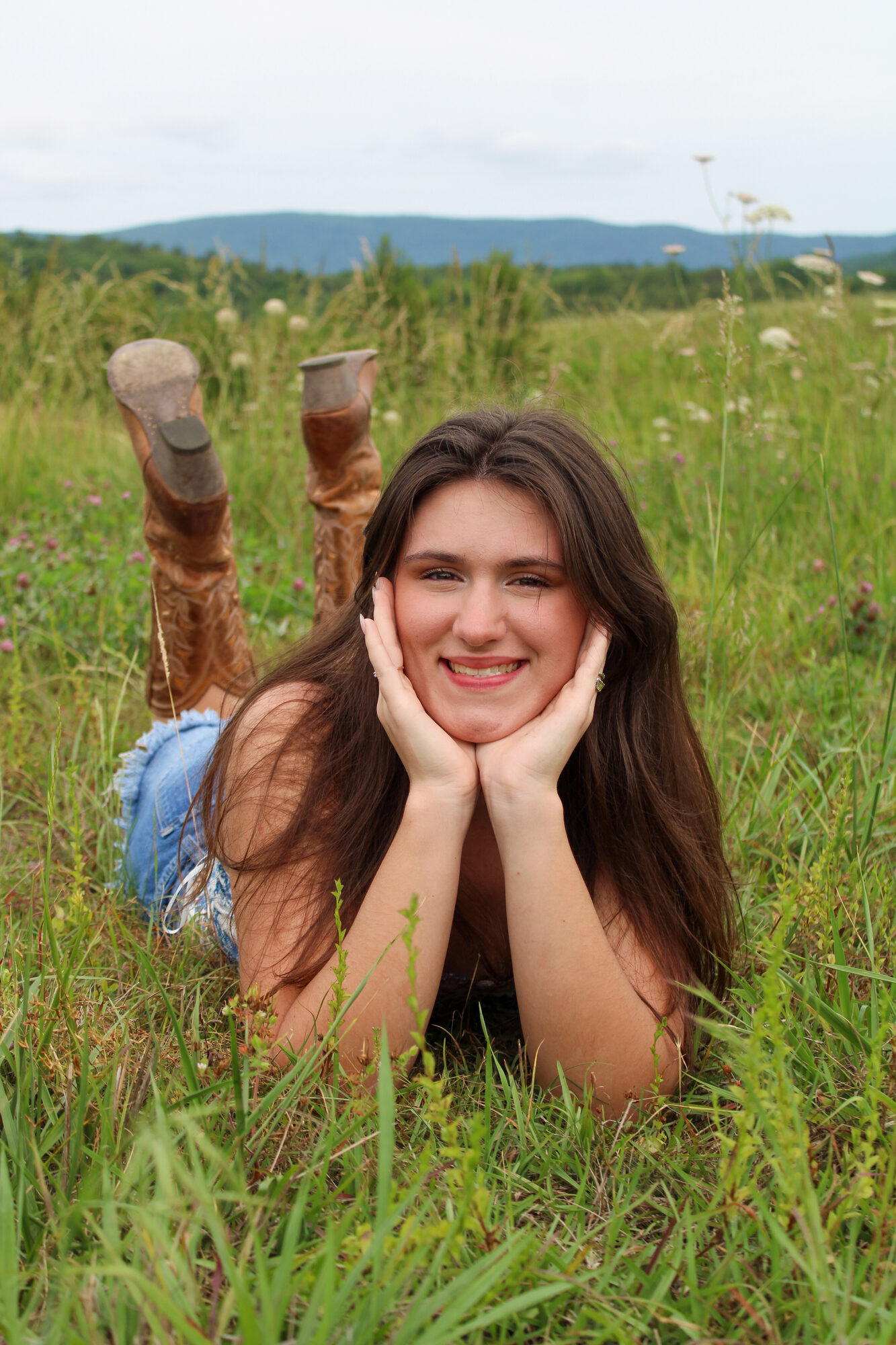 Relaxed senior portrait in a tall grass field with cowboy boots